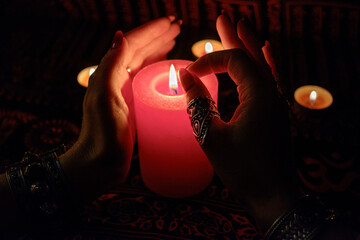 Women's hands  with bracelets and rings holding a burning candle in the dark. 