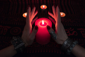 Women's hands  with bracelets and rings holding a burning candle in the dark. 