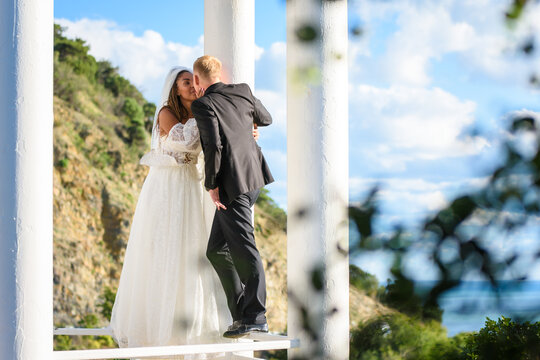 Happy newlyweds kiss in a beautiful gazebo with columns against the backdrop of foliage and sky