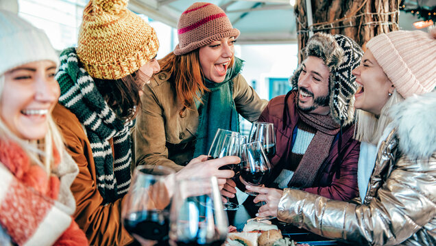 Friends group with hats and scarves toasting with glasses of red wine at bar restaurant - Winter holidays concept with people enjoying time and having fun drinking and eating together