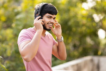 Young Indian man enjoying music with headphones at outdoors.