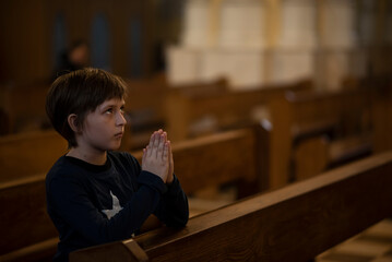 Fototapeta na wymiar a little boy in a jacket prays in a dark catholic church at a children's mass 