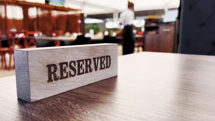 Close up of waiter putting reserved plate on table in restaurant with happy couple drinking coffee on date on blurred background. Restaurant manager placing reserved table sign. Reserved Table. 
