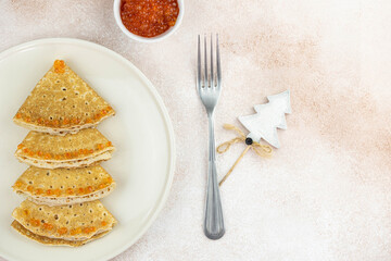 Christmas and New year tree shaped pancakes or crepes with red caviar decorations on light colored background. Holiday homemade food. Flat lay top view. Christmas food for children and kids.