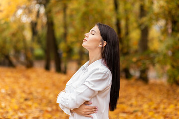 Pretty office worker (woman) closes her eyes and breathes fresh air in autumn park during lunch time, walking outdoors. Relaxation, solitude with nature. Stress relief, mental health. Horizontal plane