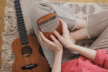 Fototapeta premium happy woman plays kalimba and ukulele and is resting at home. A successful female musician gives music lessons online. Learn to play musical instruments and sing. home office for work. small business