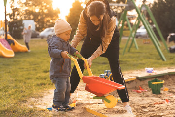 Mother and child playing with wheelbarrow in sandbox. Little builder. Education, and imagination,...