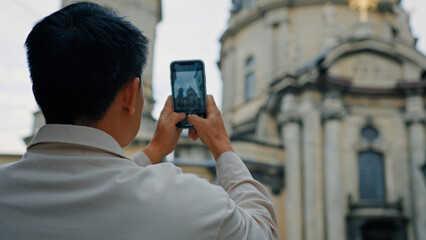 Back view unrecognizable man tourist travels in Europe photographing landmark using camera of mobile phone male blogger traveler holding smartphone taking pictures historical building in city center