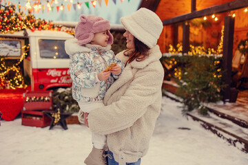 mother and daughter are walking in the christmas market and eating cookies. Merry Christmas. Walk outside on a decorated street. Holiday Market. Winter fairy tale for children