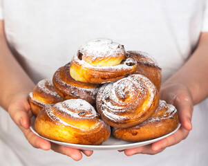 Cinnamon and raisin buns, sprinkled with powdered sugar on top on a white plate. Homemade baked goods.