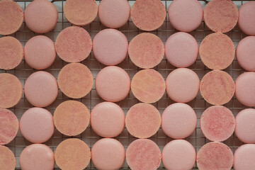 A lot of pink macaroon halves on a cooling rack. Сooking process of French dessert macaroon with strawberry flavor. Flat lay