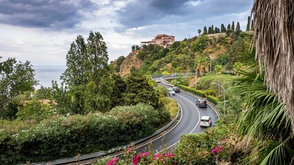 Road surrounded by green trees and plants with cars driving in Taormina, Sicily, Ital