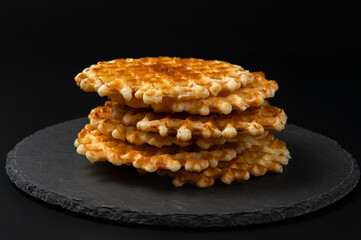 Fresh crispy Belgian waffles with a golden crust on a black stone plate on a black background