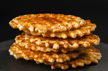 Fresh crispy Belgian waffles with a golden crust on a black stone plate on a black background close-up