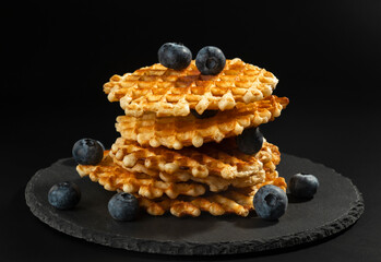 Fresh crispy with a golden crust Belgian waffles with blueberries on a black stone plate on a black background