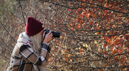 Obraz premium Kobieta fotograf, blond włosy wykonująca zdjęcia przyrody jesienią.