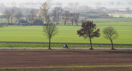 Motocykl jadący drogą na tle zielonych pól. © Adam Sadlak