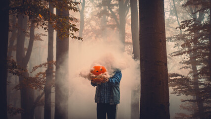 Man holding a halloween pumpkin with smoke coming out in the forest