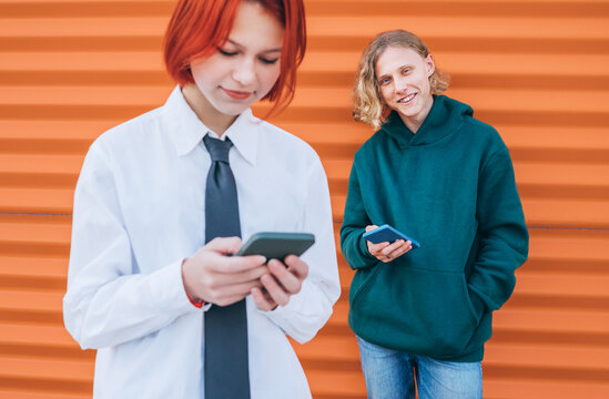 Smiling caucasian teens friends boy and a girl portraits browsing their smartphone devices. Careless young teenhood time and a modern technology concept image.