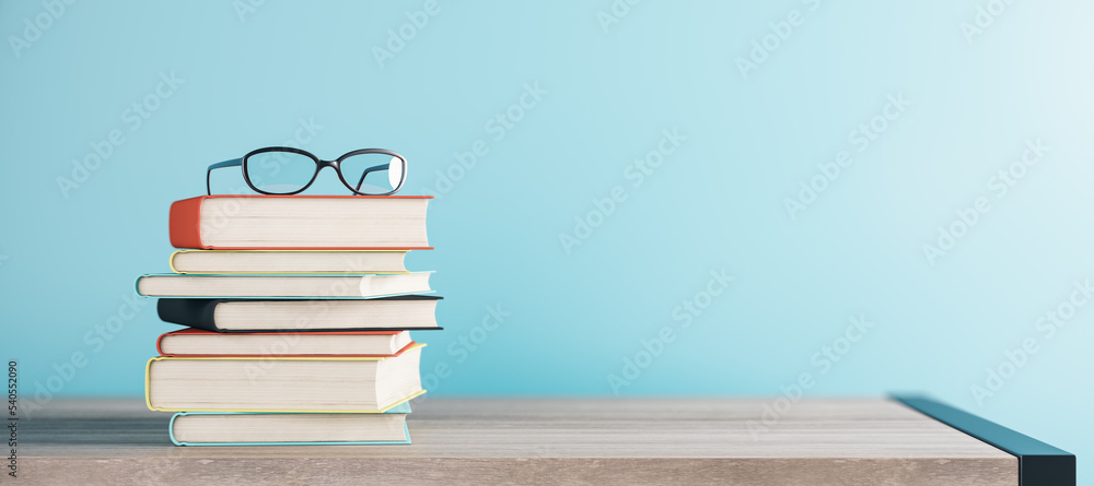 Poster close up of stacked books and glasses on blurry blue backdrop with mock up place. school and educati