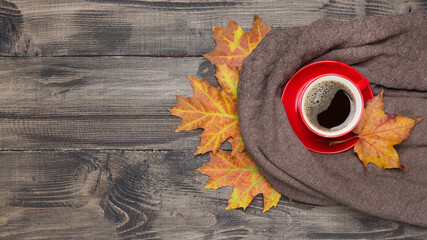 Wooden background with autumn concept, red cup with coffee and yellow leaves on a wool sweater