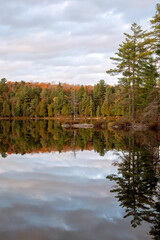 An autumn colored forest reflects on a calm lake. Pincher Lake, Algonquin Provincial Park, Ontario, Canada.