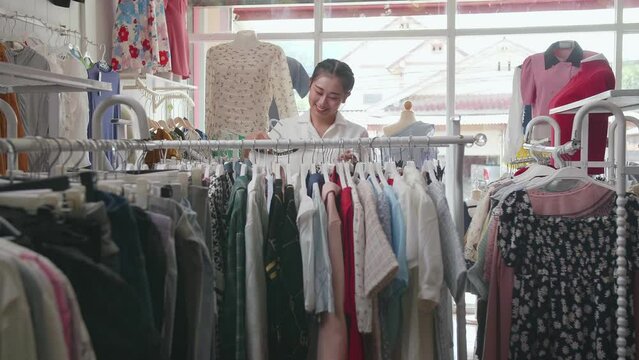 Asian Female Owner Of Clothing Store Hanging The Dresses On The Rail While Checking Stock In The Store
