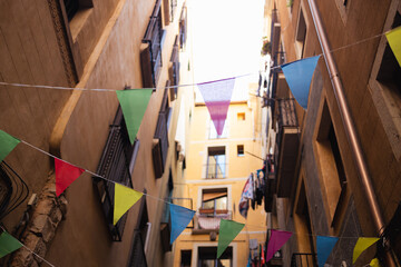 Fototapeta na wymiar Colorful triangular flag garlands hanging over a busy street on Valencia, Spain. Green, yellow and red buntings as outdoor decoration.