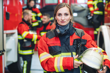 Beautiful fire fighter woman with her helmet in hand standing in the firehouse - 540557271