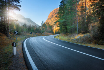 Road in autumn forest at sunset in Dolomites, Italy. Beautiful mountain roadway, orange tress,...