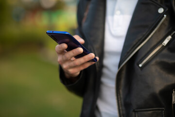 Closeup image of an unrecognizable young man holding mobile phone in hand, blurred background