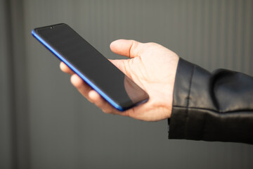 Closeup image of an unrecognizable young man holding mobile phone in hand, blurred background