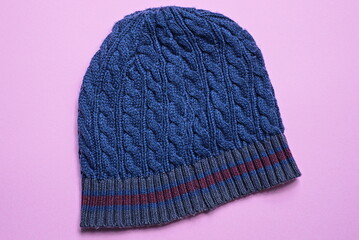 one blue wool knitted winter hat with a red stripe lies on a pink table