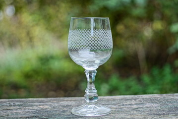 one empty white large glass goblet stands on a gray table on the street against the background of green vegetation