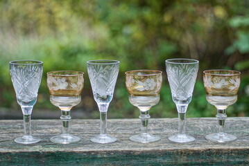 a row of white and brown glass crystal goblets on a gray wooden table outdoors on a green background