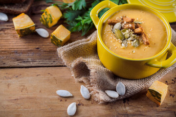 Bowl of pumpkin cream soup, bread and herbs on a wooden Board and burlap