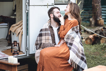 Young beautiful loving couple travelling across country in the van. Millennial man and woman in a travel camper. Cozy atmosphere, vacations vibe. Drinking tea, cooking marshmallow on a campfire