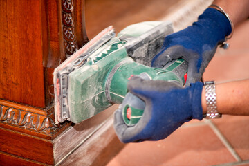 A Woman using a grinder removes old paint from furniture, restoration of antique furniture....