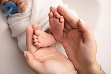 The palms of the parents. A father and mother hold the feet of a newborn child in a white blanket on a white background.. The feet of a newborn in the hands of parents. Photo of foot, heels and toes.