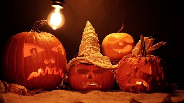 Infernal and mystical background of scary and mysterious carved Jack-o-lanterns with barn burlap and dry hay. Handmade arrangement of harvest, Halloween and spirits background with pumpkins.