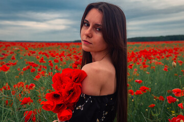 Naklejka premium Cute sexy beautiful woman in a red field of poppy flowers. Brunette girl long flowing hair. Freedom concept and tenderness