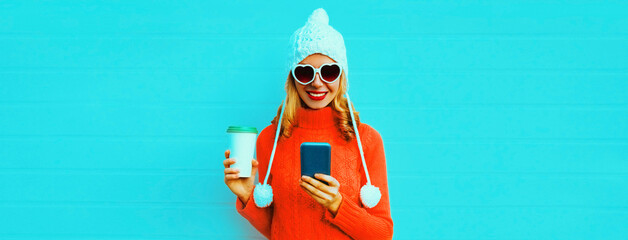 Winter portrait of happy smiling young woman with smartphone and coffee cup wearing red knitted...