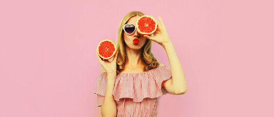 Summer portrait of beautiful young woman with slice of juicy grapefruit blowing her lips sending...