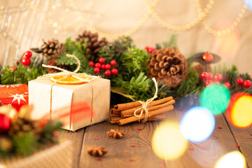 Close-up of a box with a gift wrapped in kraft paper and a Christmas background with a Christmas tree decorated with decorative balls with golden lights on a wooden table, cinnamon sticks, copy space.