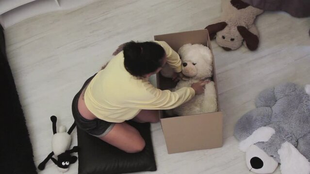 Young woman puts children's soft toys into a large box for shipping