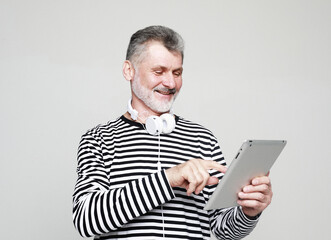Charming elderly man communicates with friends using a digital tablet and headphones.