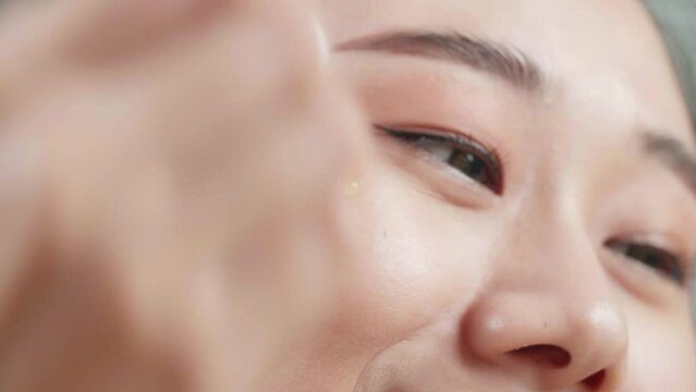 Close Up Of Beautiful Young Asian Woman Applying Serum And Smiling While Wearing Makeup At Home
