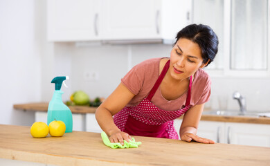 Obraz na płótnie Canvas Asian woman householder using rag to polish kitchen table. Cleanup in apartment.