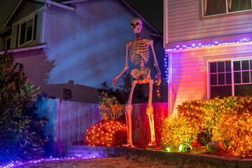 Illuminated night Halloween house outdoor decorations with garlands and skeleton near the house