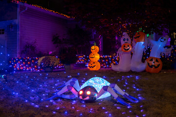 Glowing Halloween outdoor decorations with inflatable spider, pumpkins, ghosts and blue garlands in the house yard